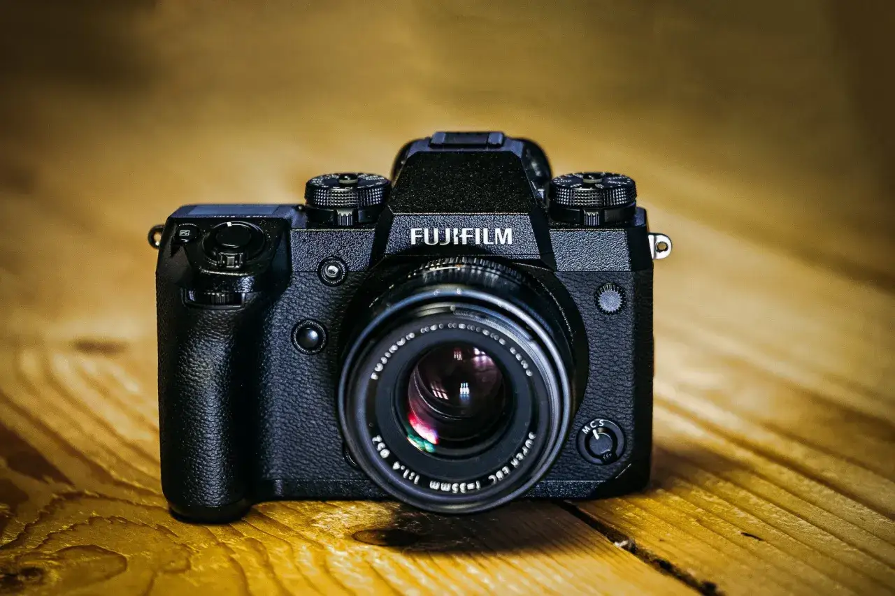 Profesjonalny aparat Fujifilm X-H1 z obiektywem na drewnianym tle.