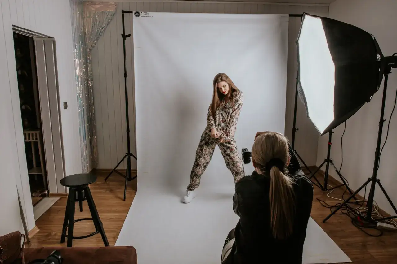 Sesja fotograficzna modowa: modelka w kwiecistym kombinezonie pozuje do zdjęcia, fotografka z aparatem w ręku.