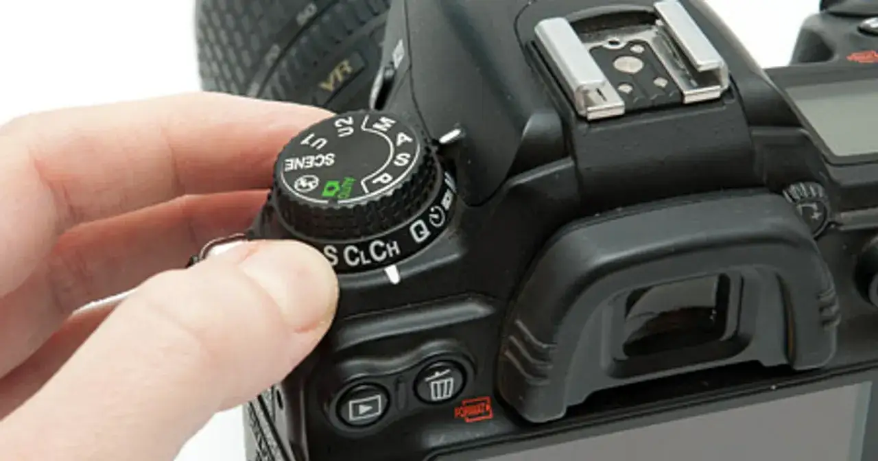 Dłoń obraca pokrętło tryb&oacute;w aparatu Nikon D7000, pokazując jego dane techniczne i możliwości.