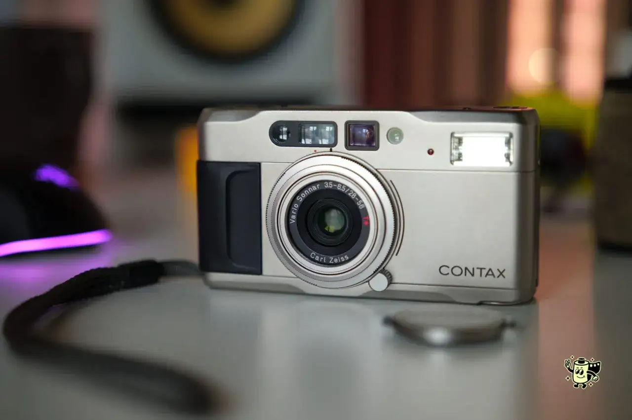 Srebrny aparat Contax TVS z obiektywem Carl Zeiss Vario-Sonnar. Na stole leży też smycz i świecąca na fioletowo myszka.
