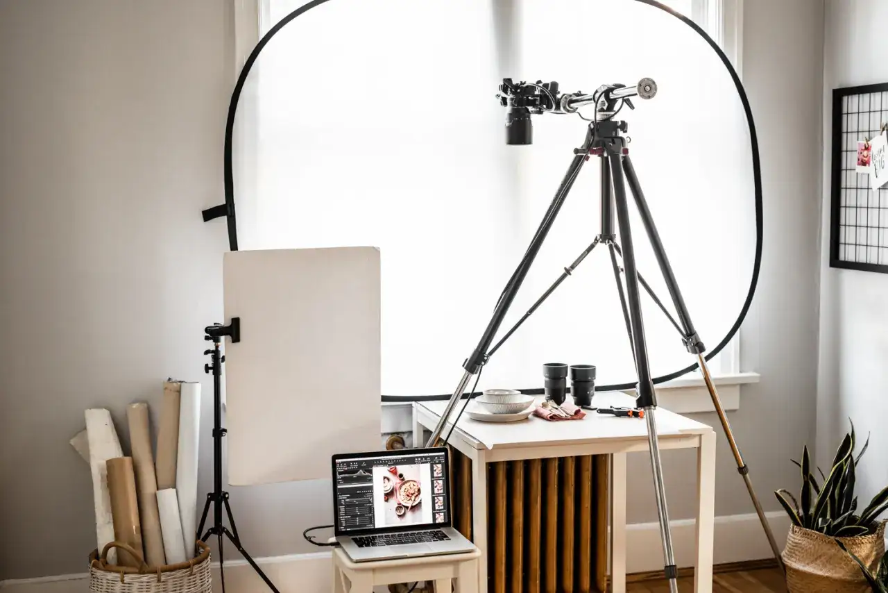 Studio do tworzenia zdjec wnetrz: statyw z aparatem, laptop z edytorem, tło, talerze i kosz z rolkami papieru.