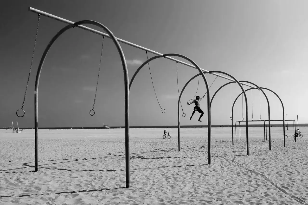 Kompozycja dynamiczna fotografia: człowiek w powietrzu na k&oacute;łkach gimnastycznych, rowerzysta na piasku, plaża i morze w tle.